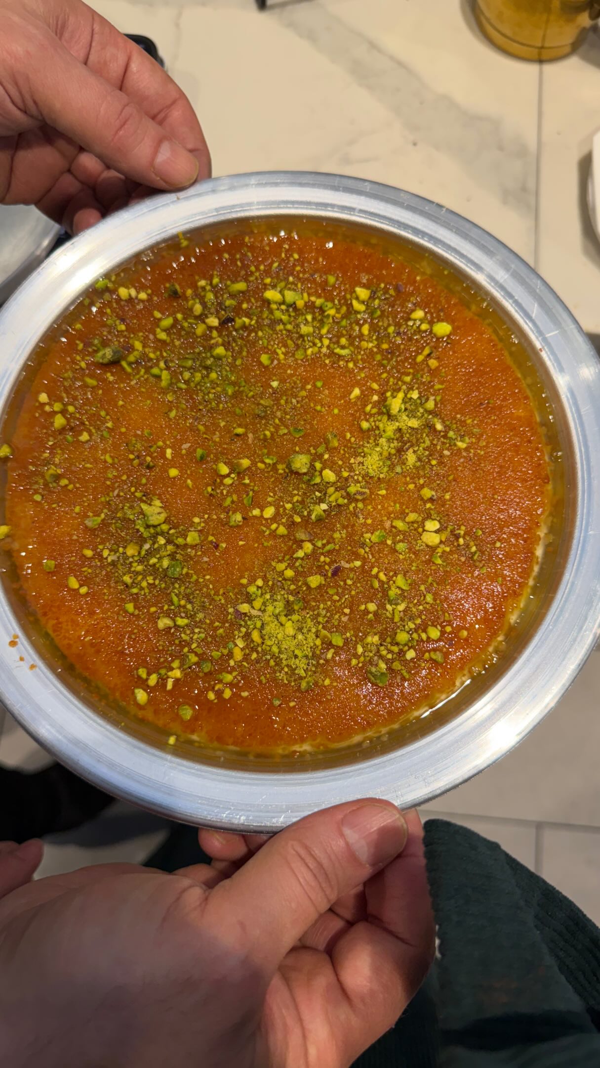 Fresh knafeh pan dusted with pistachio — held and ready to serve