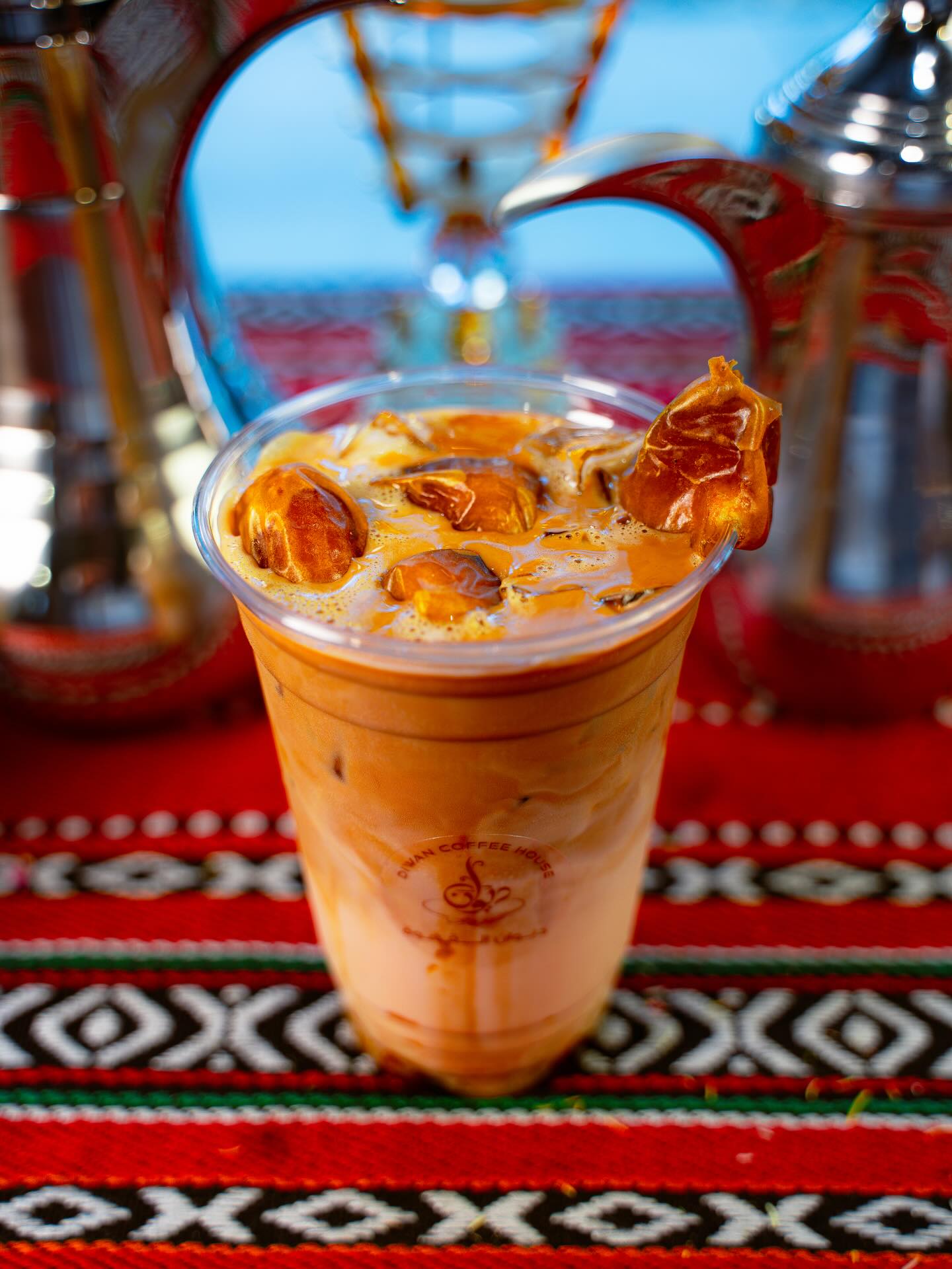 Iced caramel date latte on Palestinian tablecloth with traditional dallah pitchers